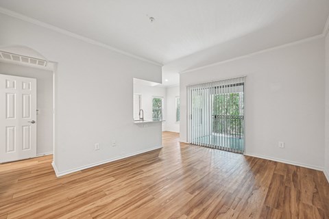 the living room and dining room of an apartment with wood flooring and a balcony
