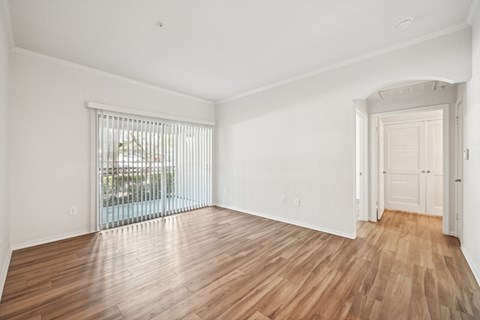 a living room with white walls and wood flooring and a door to a balcony