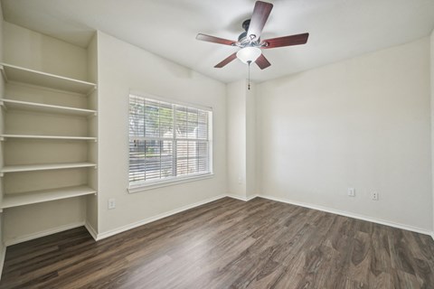 an empty living room with a ceiling fan and shelves