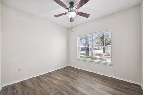 the living room of an apartment with a large window and a ceiling fan