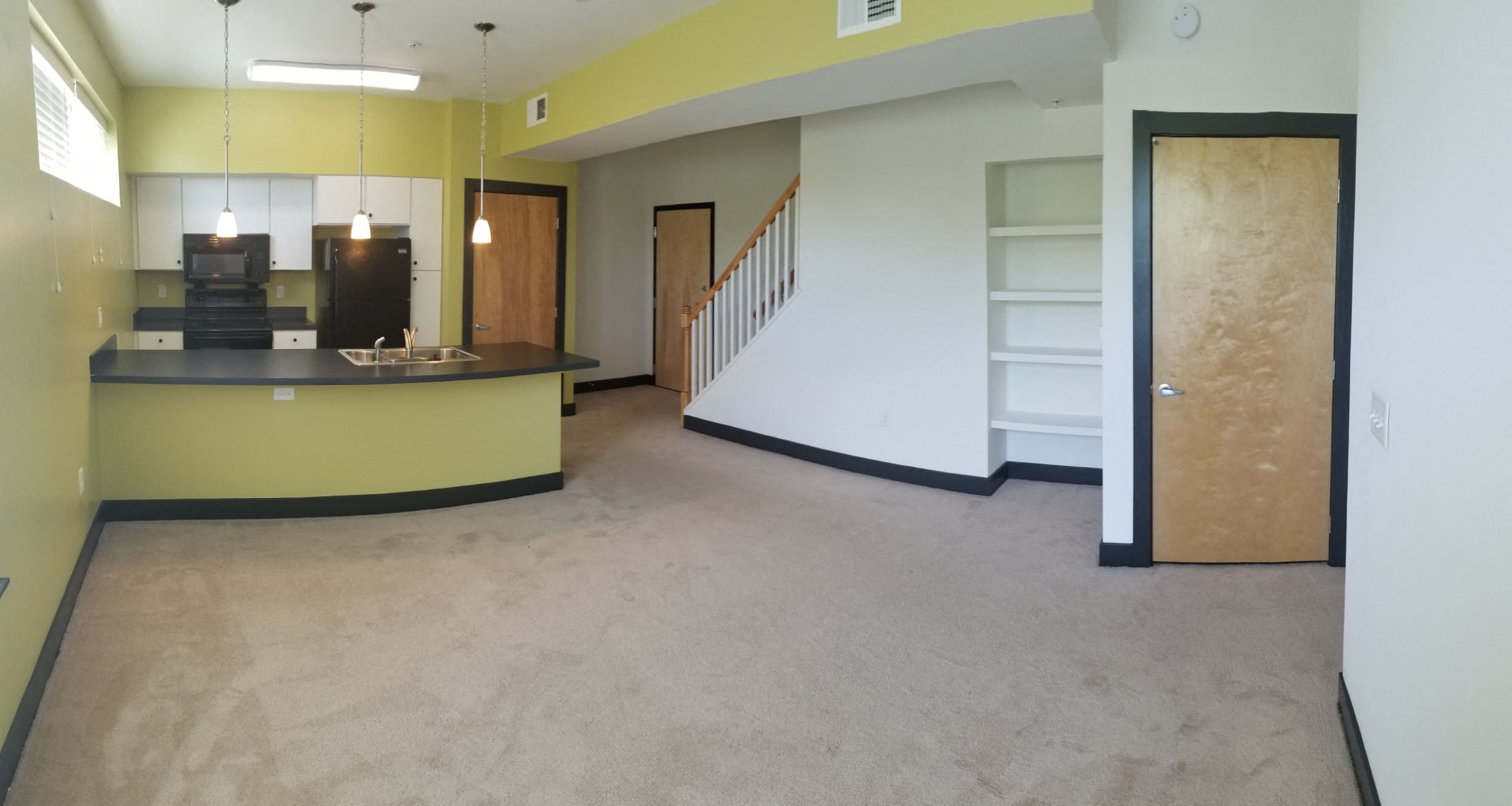 an empty living room with a kitchen and a staircase