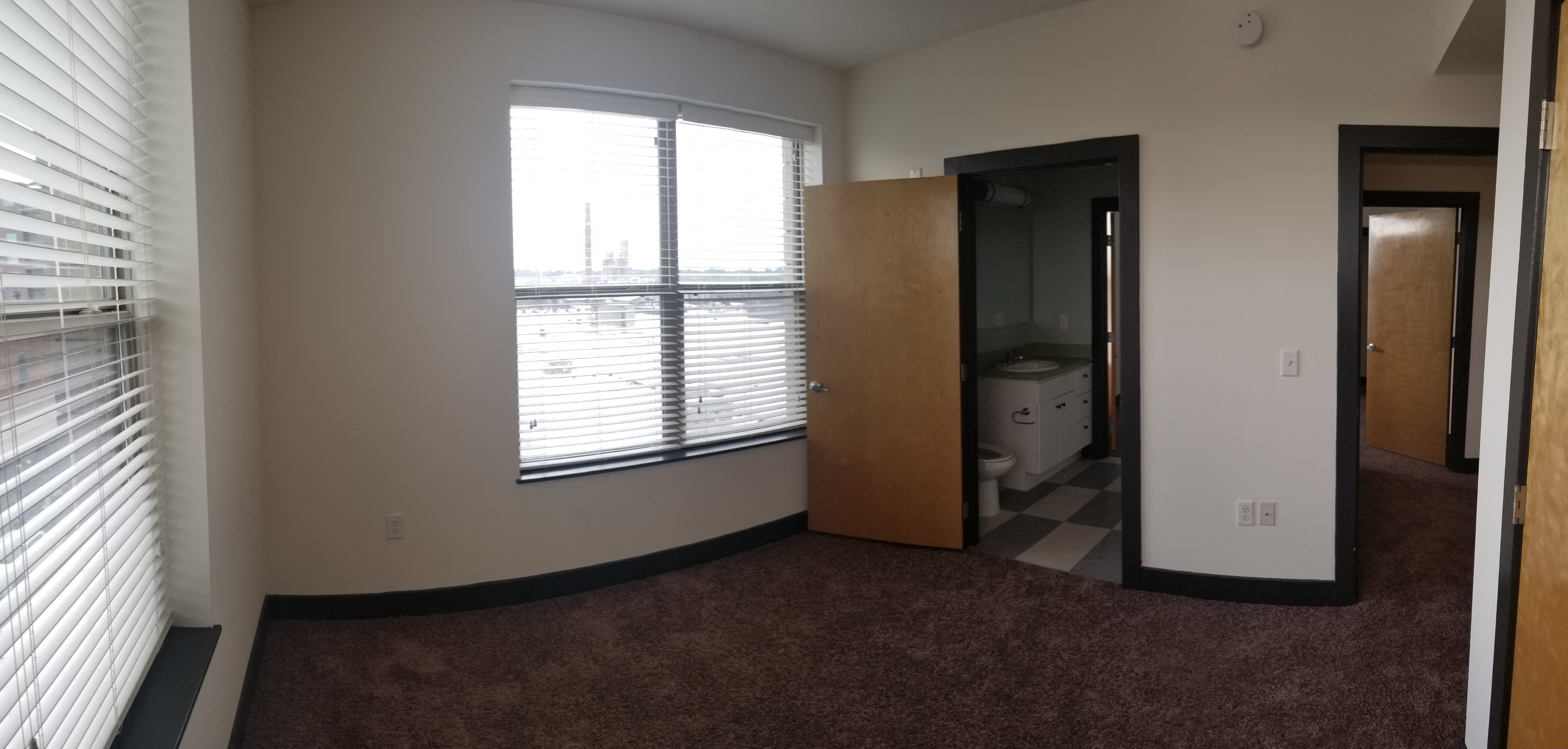 an empty living room with a large window and a door to a bathroom
