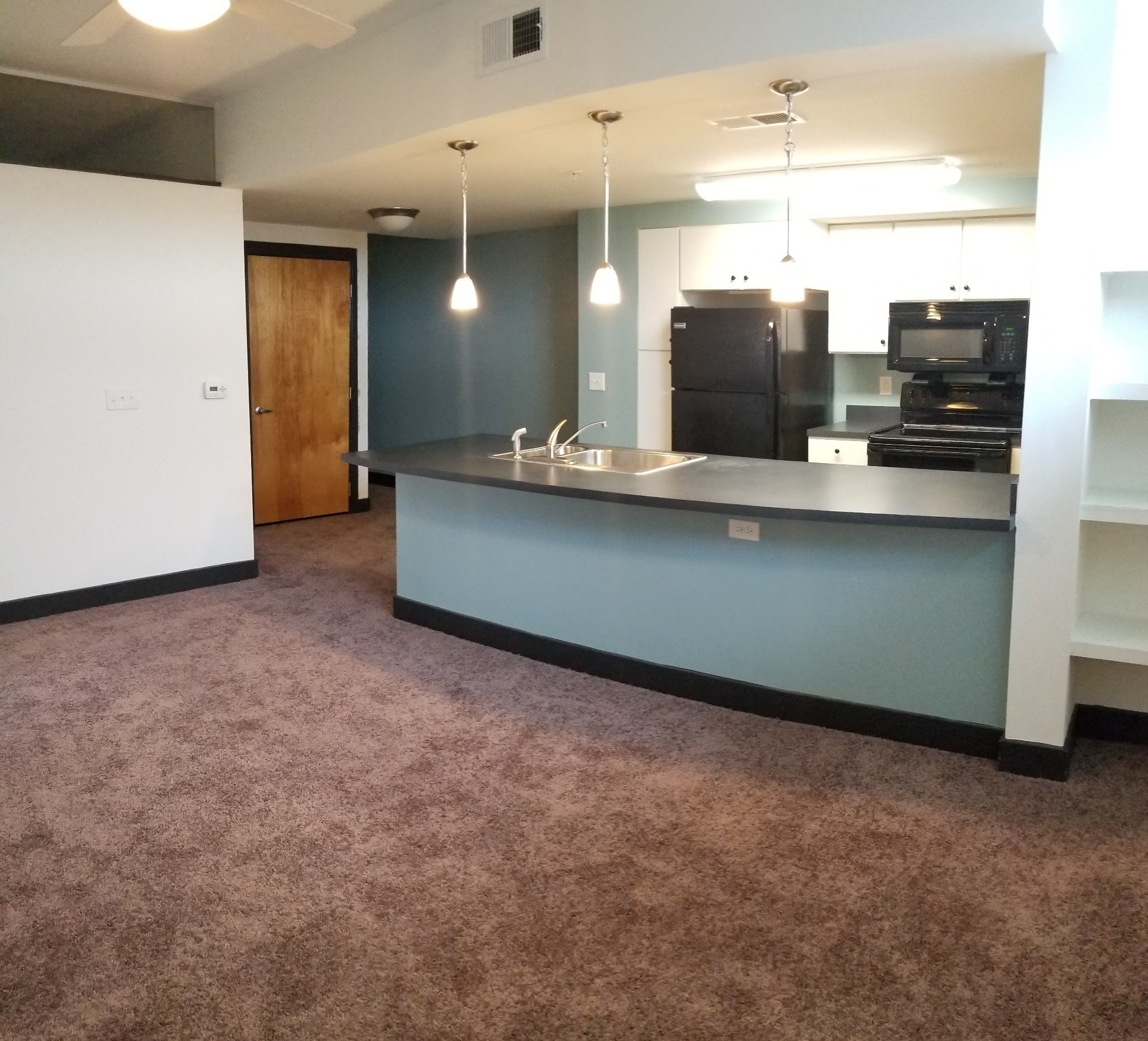 an empty living room with a kitchen with a blue counter top