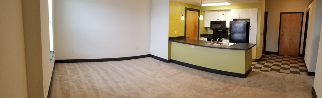 an empty living room with a kitchen and a checkered floor