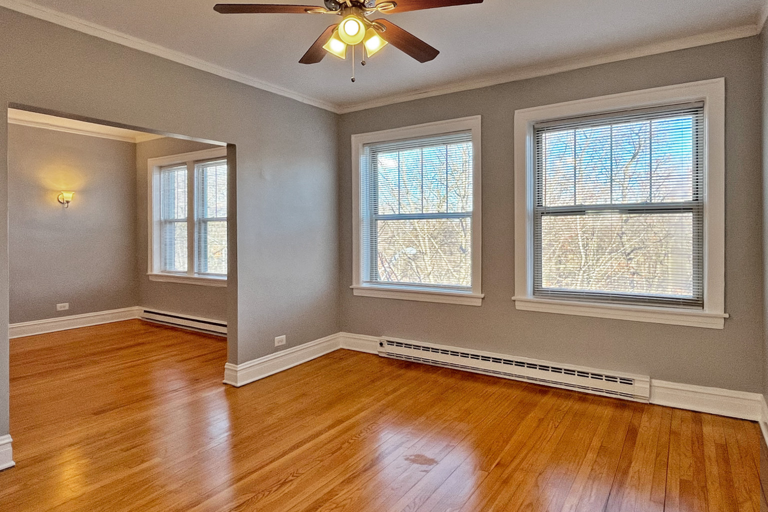 A room with a ceiling fan and two windows.