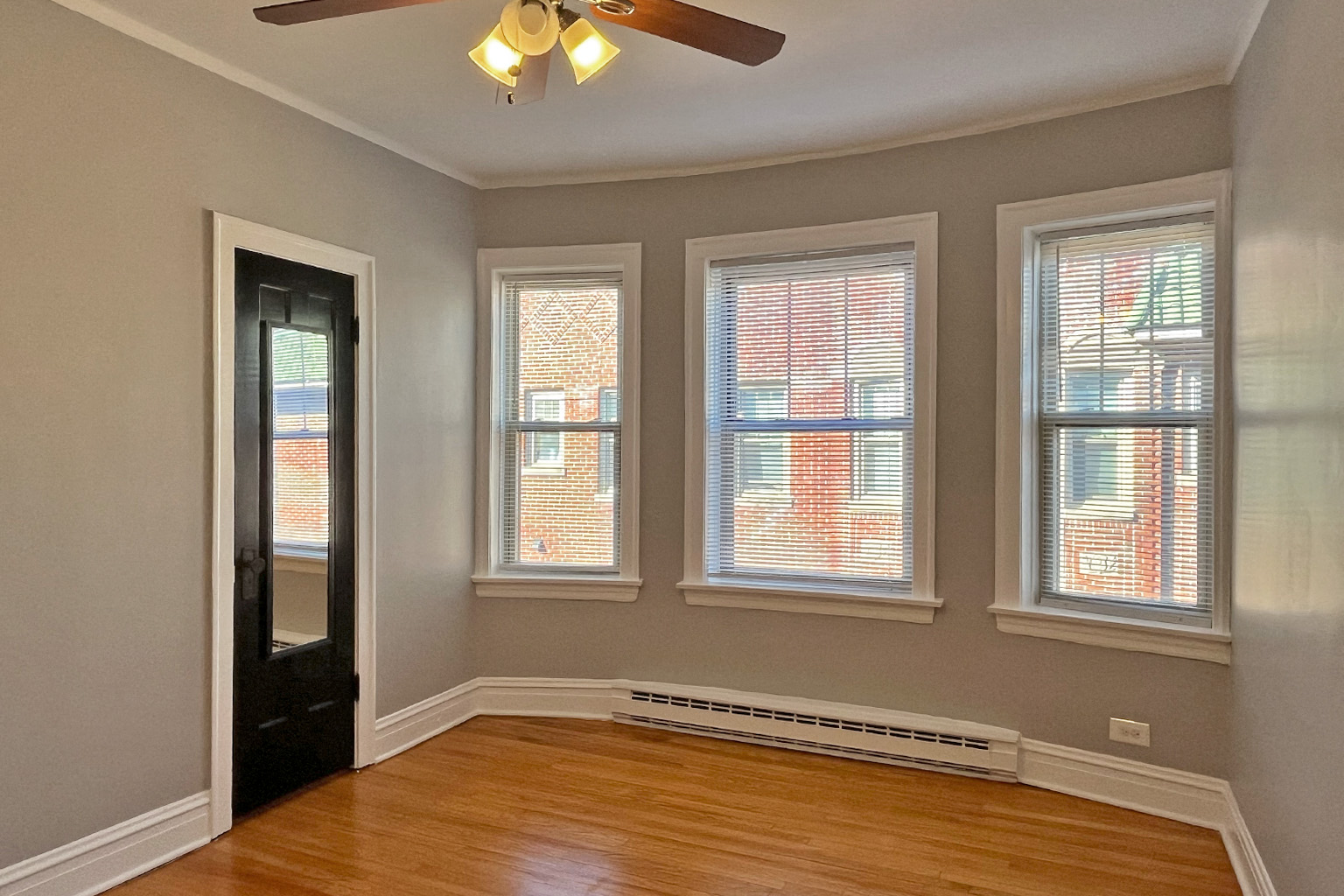 A room with a ceiling fan and three windows.