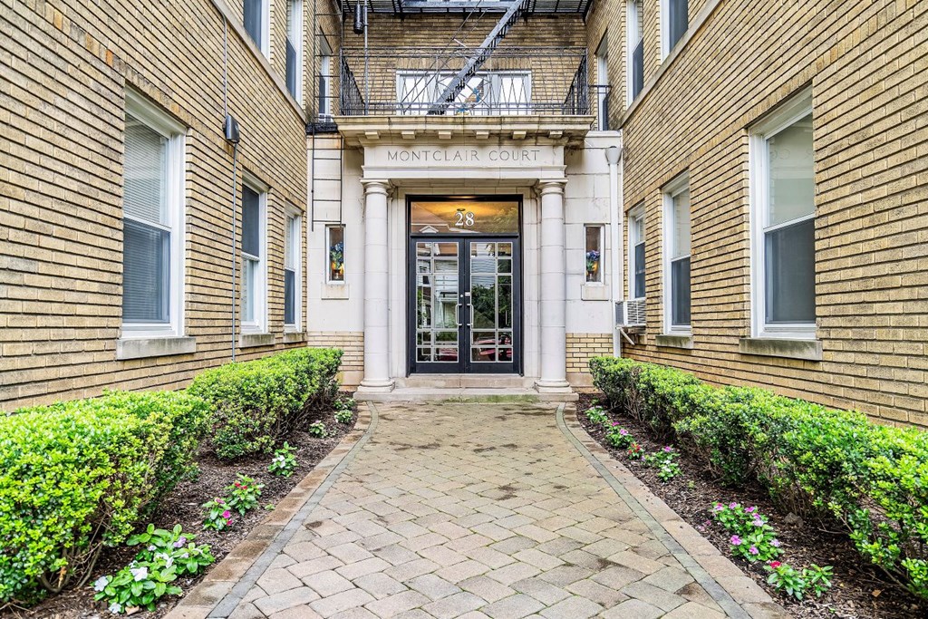 the front entrance of a condo building with a brick walkway and manicured gardens