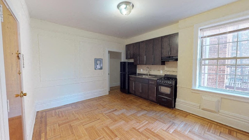 an empty kitchen with a wooden floor and a black refrigerator