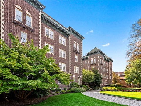 the front of a brick building with a garden and a pathway