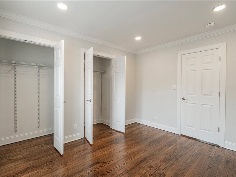 A room with white walls and wooden floors, with two open doors.