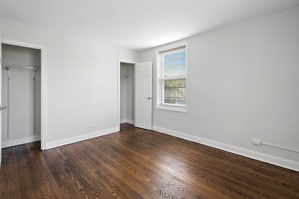 a bedroom with white walls and wood flooring and a closet