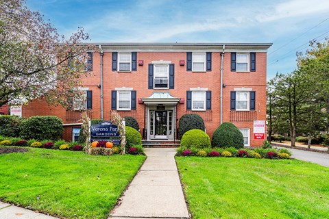 the front of a brick building with a green lawn and a sidewalk