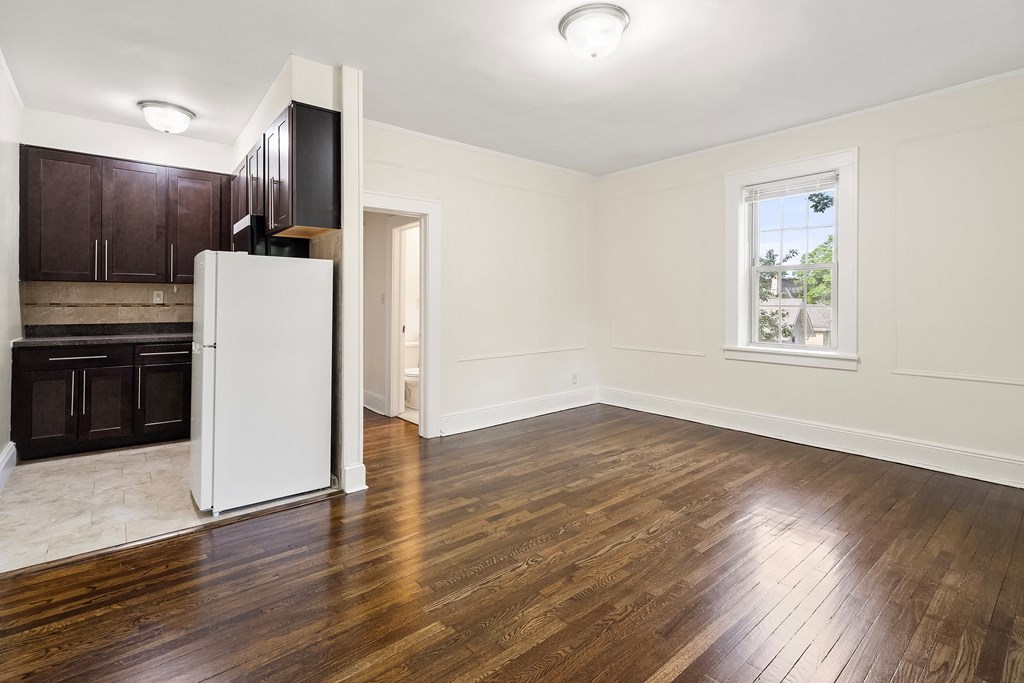 an empty living room with wood floors and a white refrigerator