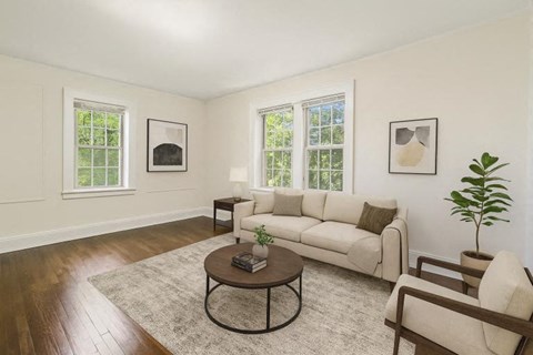 A living room with a white couch, a coffee table, and two windows.