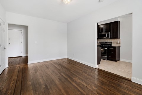 an empty living room with wood flooring and a kitchen