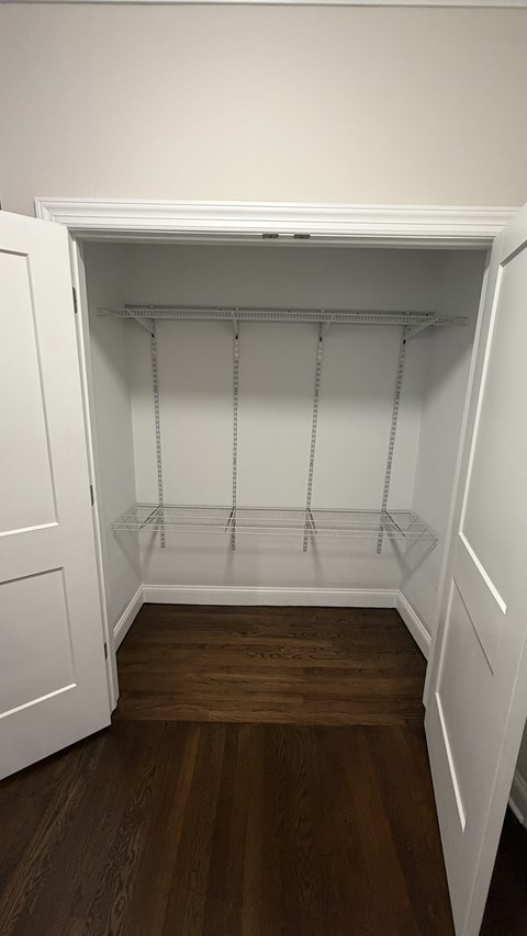 A white closet with wooden floors and shelves.