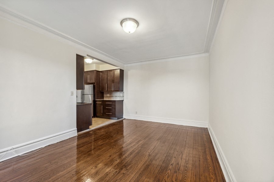 an empty living room with wood flooring and a kitchen