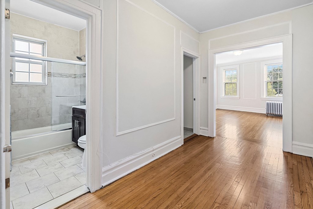 an empty room with white walls and wood floors and a bathroom with a glass shower