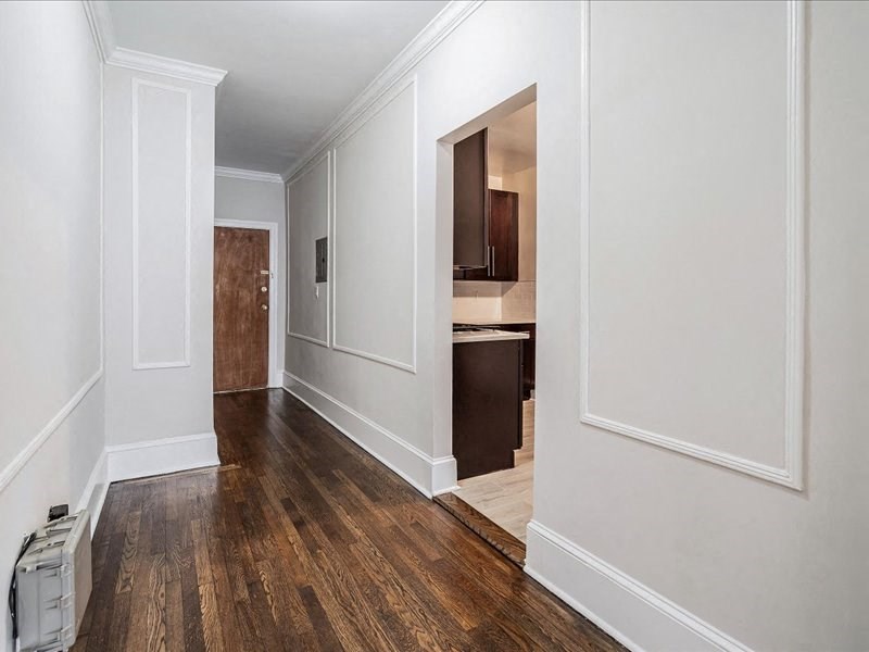 a hallway with white walls and wood flooring and a doorway to a kitchen