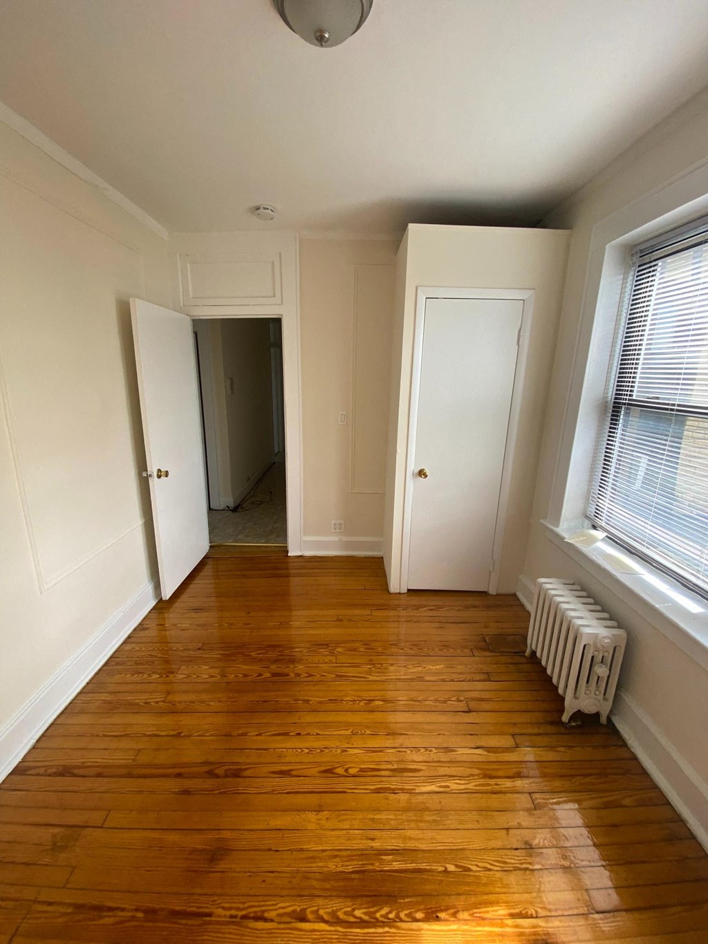 a small room with a wood floor and a window and a radiator