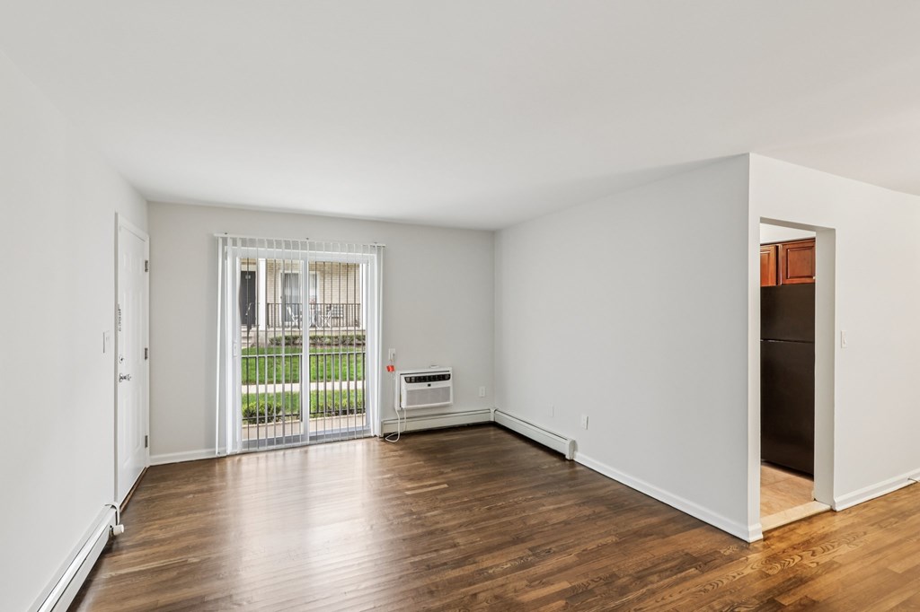 A room with white walls and wooden flooring, with a window and a door leading outside.
