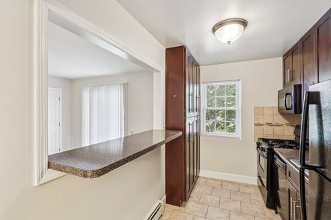 A kitchen with a black refrigerator and a window with white curtains.
