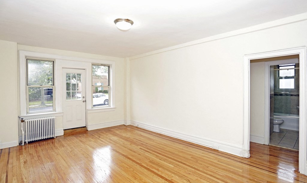 an empty living room with wood floors and a door to a bathroom