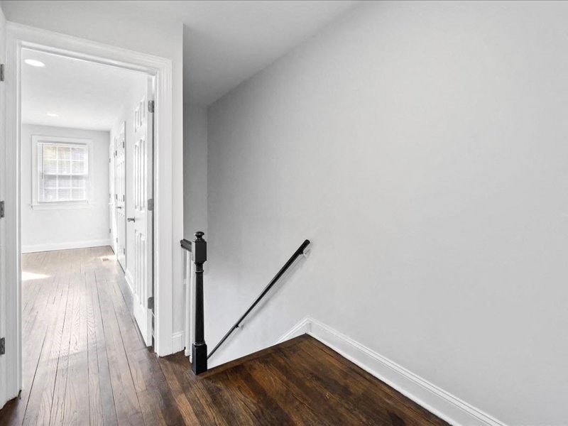 a hallway with white walls and wood flooring and a railing on the wall