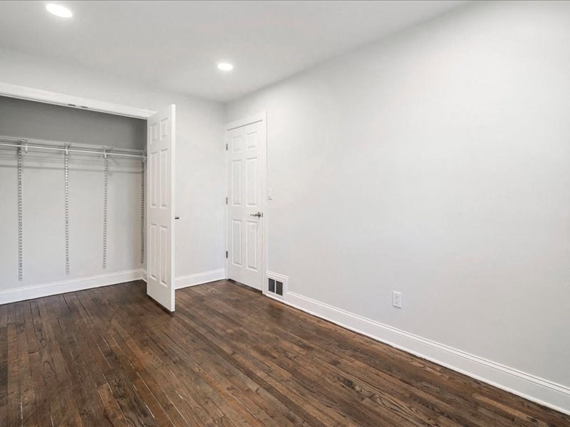 a bedroom with white walls and wood flooring and a closet