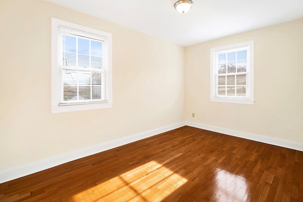 an empty room with wood floors and two windows