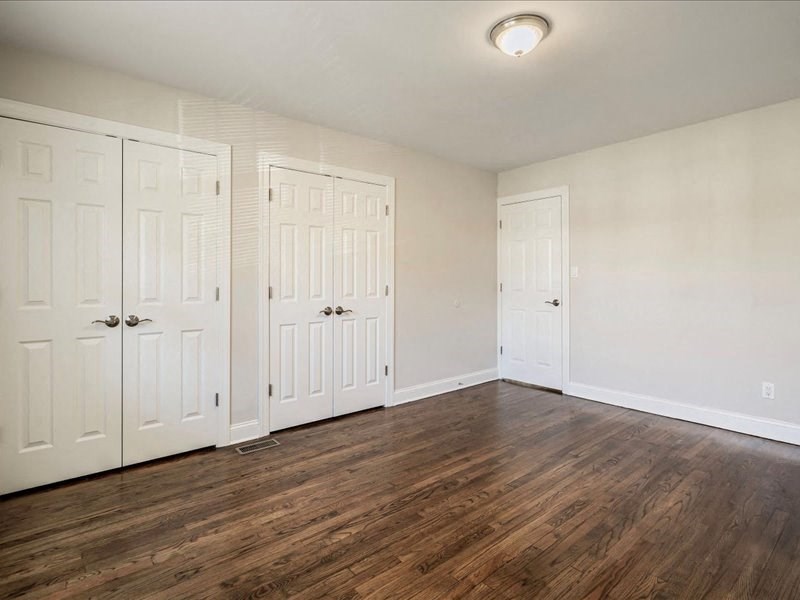 an empty bedroom with white doors and wood flooring