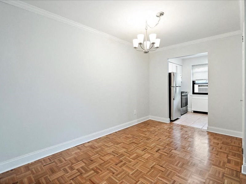 an empty living room with wood flooring and a refrigerator