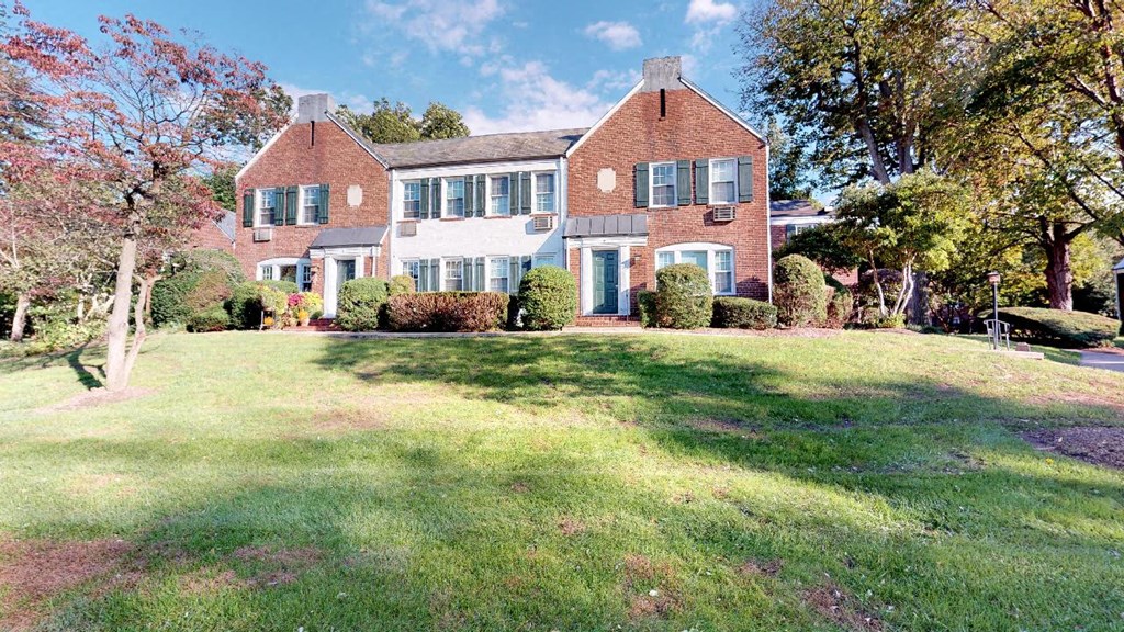 a large brick house with green shuttered windows and a lawn in front