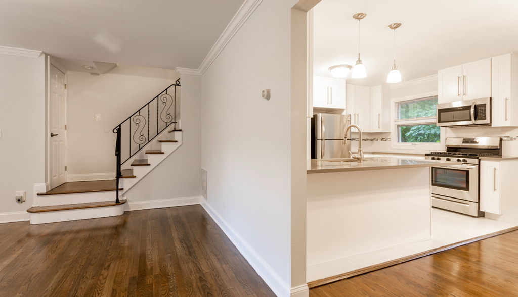a living room with a staircase and a kitchen with white cabinets
