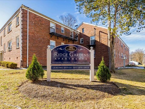 A sign for Ridge Gardens Apartments in front of a brick building.