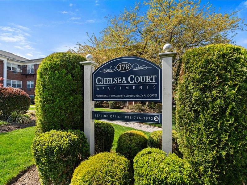 A sign for Chelsea Court Apartments stands in front of a building.
