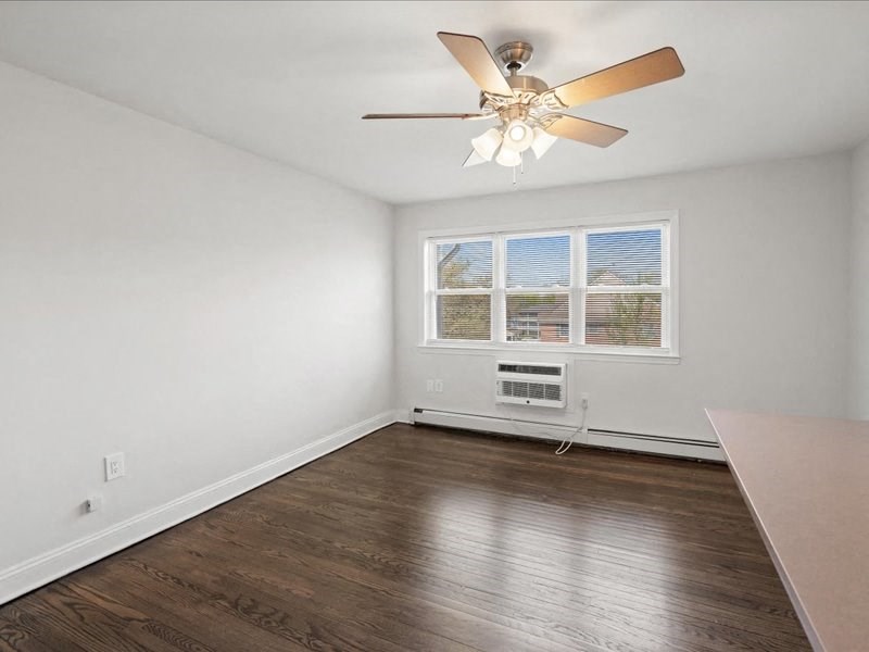 A room with a ceiling fan and a window with an air conditioner unit underneath it.