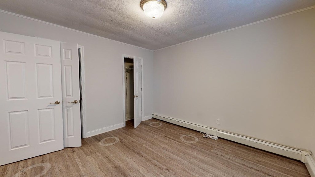 a bedroom with white walls and wood flooring and a closet
