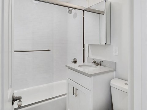 A white bathroom with a sink, mirror, and bathtub.