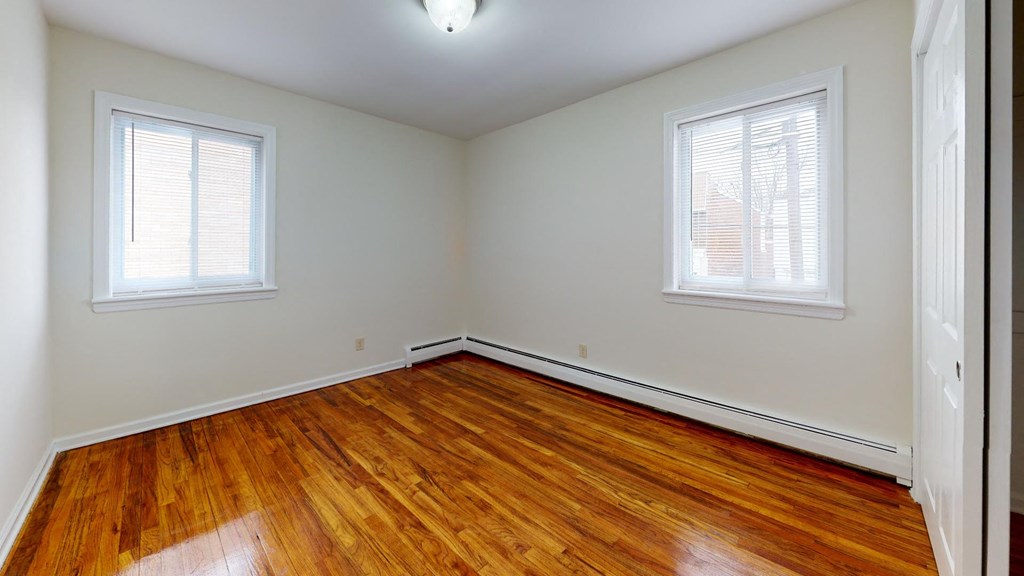an empty room with wood floors and two windows