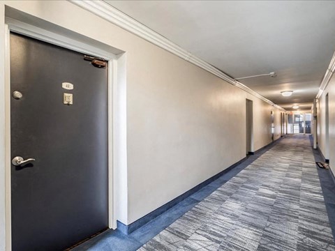 A hallway with a black door on the left and a grey carpeted floor.