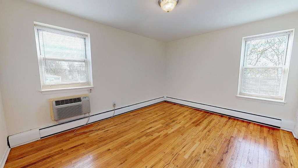 an empty room with wood floors and a radiator and two windows