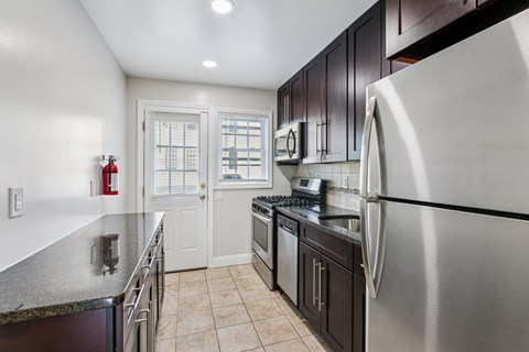 A modern kitchen with a stainless steel refrigerator, black countertops, and white cabinets.