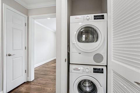 A white door is open to a hallway with a stack of white washing machines.