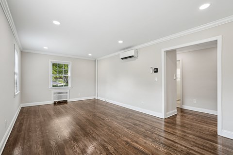 A room with wood flooring and a window with a view of trees and a white air conditioner on the wall.