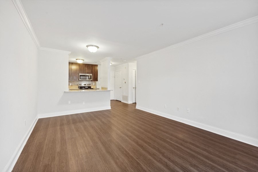 the living room and kitchen of an apartment with white walls and wood flooring