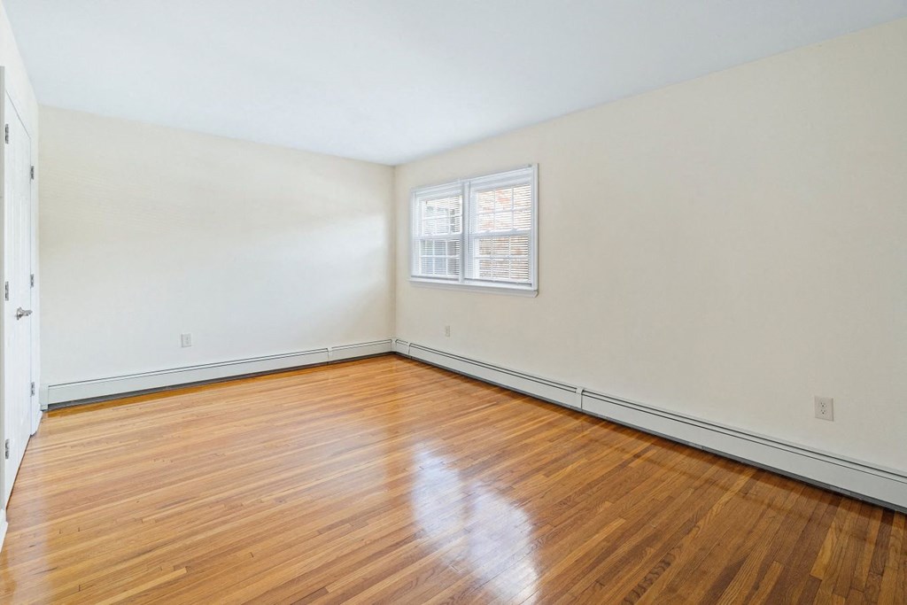 an empty room with wood floors and white walls and a window