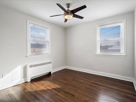 A room with a ceiling fan and two windows.