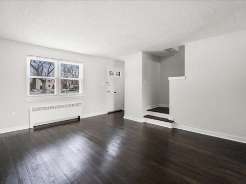 A room with a white door and a window with a view of a house and trees.