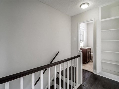 A white hallway with a black railing and a doorway leading to another room.